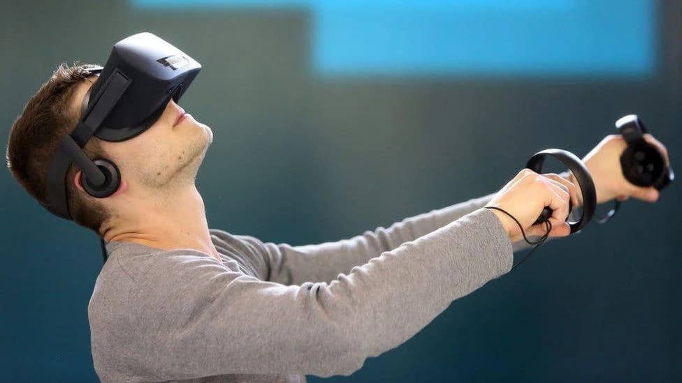 Man wearing a VR headset and holding motion controllers, reaching out inside an immersive video experience
